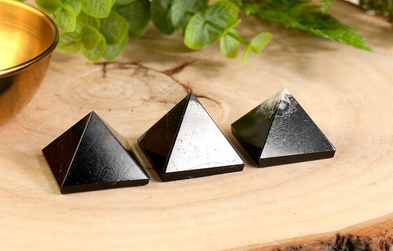 May include: Three black obsidian pyramids of varying sizes on a wooden surface. The pyramids are smooth and polished.