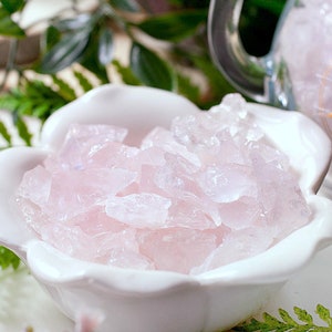 May include: A white ceramic bowl shaped like a flower with pink rose quartz crystals inside.