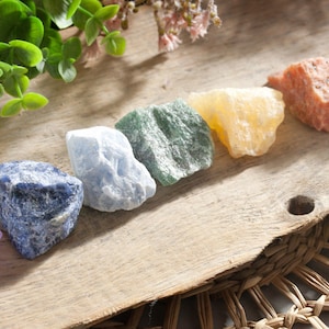 Könnte beinhalten: Sieben Chakra-Steine, die in einer Reihe auf einer Holzoberfläche angeordnet sind. Die Steine sind Amethyst, Sodalith, blauer Spitzenachat, grüner Aventurin, Citrin, Karneol und roter Jaspis.