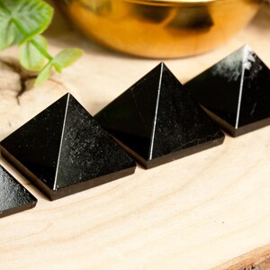 May include: Four black obsidian pyramids arranged in a row on a wooden surface. The pyramids are smooth and polished, with a slight sheen.