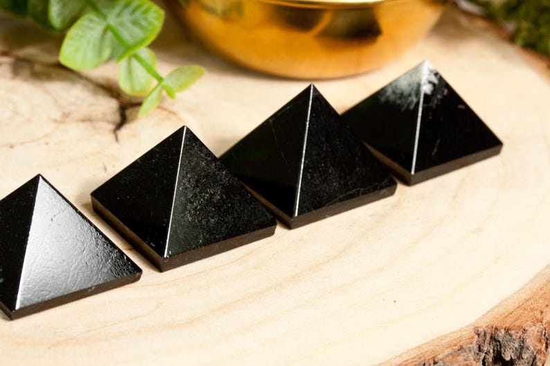 May include: Four black obsidian pyramids arranged in a row on a wooden surface. The pyramids are smooth and polished, with a slight sheen.