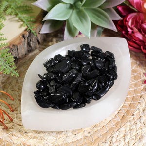 Könnte beinhalten: Eine weiße Schale gefüllt mit schwarzen Obsidian-Chips. Die Schale steht auf einer geflochtenen Strohmatte.