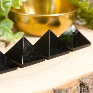 May include: Four black obsidian pyramids arranged in a row on a wooden surface. The pyramids are smooth and polished, with a slight sheen.