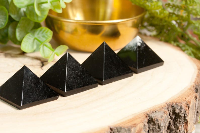 May include: Four black obsidian pyramids arranged in a row on a wooden surface. The pyramids are smooth and polished, with a slight sheen.