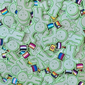 Può includere: Una collezione di adesivi fustellati raffiguranti un personaggio dei cartoni animati verde pallido con un'espressione semplice. Ogni figura tiene in mano una piccola bandiera con vari motivi pride, inclusi disegni arcobaleno, bisessuali, transgender e non binari.