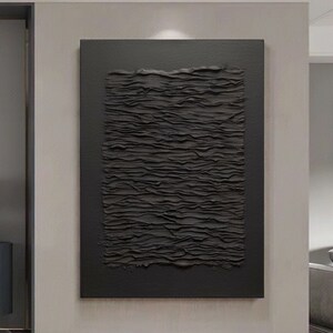 Può includere: Un dipinto astratto in bianco e nero con un design testurizzato e stratificato. Il dipinto è incorniciato e appeso a un muro.
