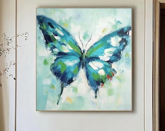 May include: A framed butterfly painting with a blue, green, and white color palette. The artwork features a large butterfly with detailed wing patterns against a soft, abstract background. The painting is displayed above a brown bench.