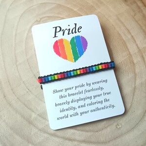 May include: A white card with the word "Pride" in black text and a rainbow heart. The card is next to a rainbow bracelet with black beads. The card reads "Show your pride by wearing this bracelet fearlessly, bravely displaying your true identity, and coloring the world with your authenticity."