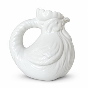 May include: A white ceramic pitcher shaped like a rooster. The vessel features a sculpted head with a comb at the top, a curved handle forming the tail, and detailed molded feathers across the body. The surface is smooth, glossy, and solid white.