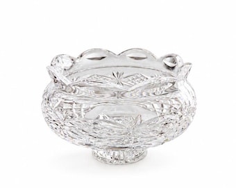 May include: A clear, colorless glass bowl featuring intricate cut patterns including cross-hatching and starburst designs. The bowl has a scalloped rim and sits on a circular pedestal base, showcasing a reflective, faceted surface throughout.