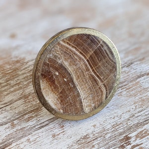 May include: A round, brown and white marble cabinet knob with a gold metal rim.