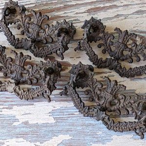 May include: Five antique ornate metal drawer pulls with a floral design. The pulls are a dark brown color and have a distressed finish.