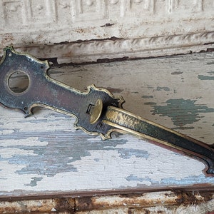 May include: Antique brass door handle with ornate details and a patina finish. The handle is designed with a long, curved lever and a decorative plate.