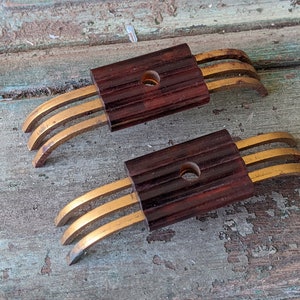 May include: Two brown and gold metal electrical connectors with three prongs each. The connectors are on a wooden surface.