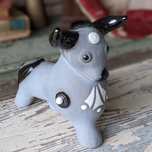 May include: A gray ceramic bull figurine with black horns and white accents. The bull has a stylized design with geometric shapes and circles.