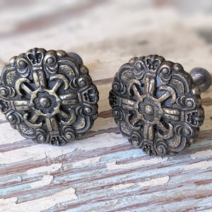 May include: Two ornate brass cabinet knobs with a detailed floral design. The knobs have a slightly aged finish and are attached to screws.