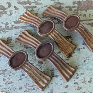 May include: Four antique bronze drawer pulls with an oval center and ribbed design. The pulls are arranged diagonally on a distressed, turquoise-painted wooden surface. These decorative hardware pieces are ideal for furniture restoration.