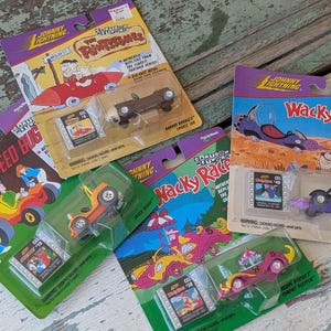 May include: A collection of Johnny Lightning die-cast toy cars, featuring cartoon characters and vehicles from The Flintstones, Wacky Races, and Speed Buggy. Each car is in its original packaging, with vibrant colors and detailed graphics.