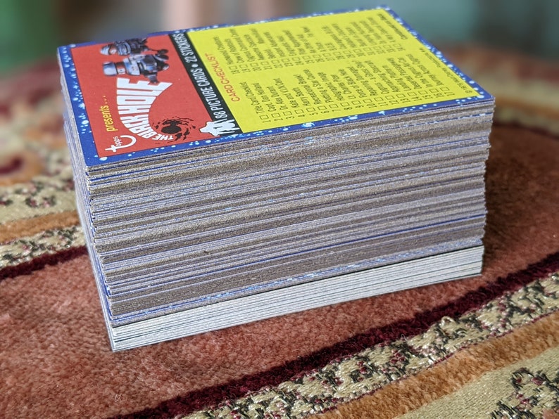 May include: A stack of trading cards featuring a cartoon image of a monster with the text "The Black Hole presents..." and "188 Picture Cards + 22 Stickers". The cards are yellow with blue and red accents.