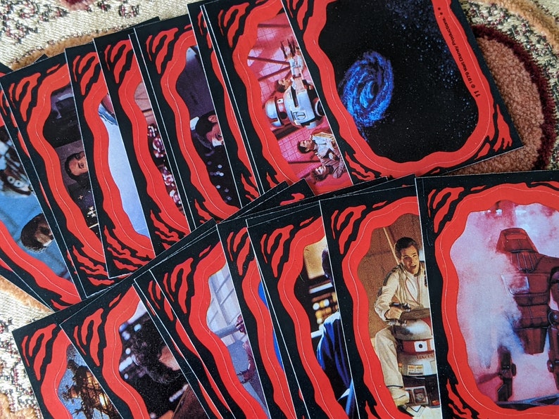 May include: A stack of trading cards with red and black borders. The cards feature images from the Star Wars movie franchise. The cards are in a variety of scenes and characters.