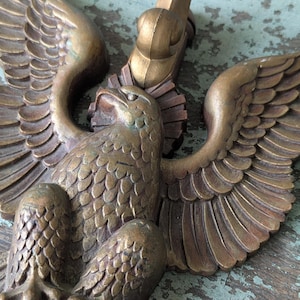 May include: A detailed bronze-colored eagle sculpture with outstretched wings. The eagle has a detailed feather pattern and is mounted on a decorative element. The sculpture is likely a wall hanging or decorative piece.