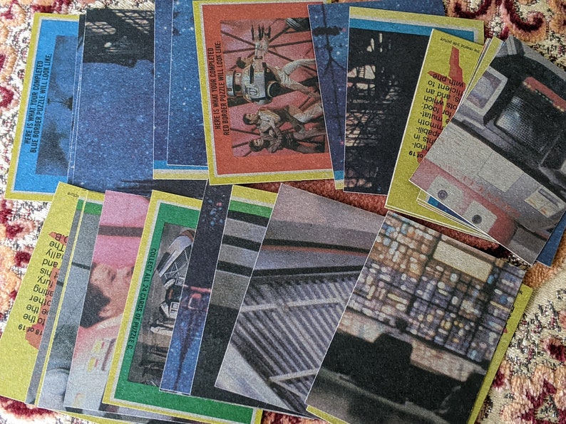 May include: A collection of 24 cards featuring images from a science fiction movie. The cards are yellow, green, and blue with a white border. The text on the cards reads "Collect all 24 cards of puzzle", "Here is what your completed red border puzzle will look like", and "Here is what your completed blue border puzzle will look like".