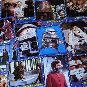 May include: A collection of trading cards featuring characters and scenes from the science fiction television series, 'Star Wars: The Clone Wars'. The cards are blue with white stars and feature images of robots, spaceships, and characters from the show. The text on the cards includes titles like 'A Truce... For Now!', 'Burial in Space', 'Apprehended!', 'An Offer of Aid', 'A Very Special Dinner', 'The Limping Humanoid', and 'Captain S.T.A.R.'