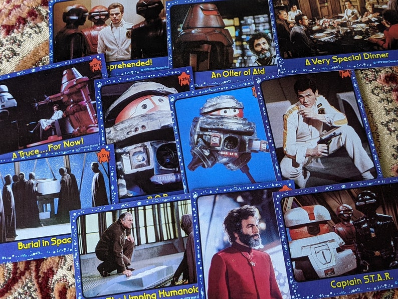 May include: A collection of trading cards featuring characters and scenes from the science fiction television series, 'Star Wars: The Clone Wars'. The cards are blue with white stars and feature images of robots, spaceships, and characters from the show. The text on the cards includes titles like 'A Truce... For Now!', 'Burial in Space', 'Apprehended!', 'An Offer of Aid', 'A Very Special Dinner', 'The Limping Humanoid', and 'Captain S.T.A.R.'