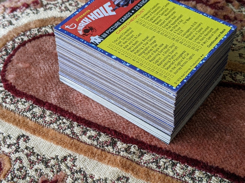 May include: A stack of 88 trading cards featuring characters and scenes from the 1979 film "The Black Hole". The cards are blue, yellow, and white with a checklist on the back.