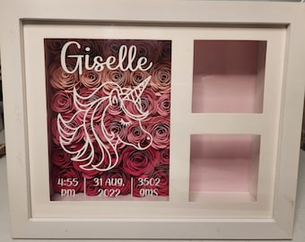 Peut inclure: Boîte à ombre en bois blanc avec un arrangement de fleurs en papier rose et rouge, une silhouette de licorne et le nom "Giselle" écrit en blanc. La boîte comprend également une petite fenêtre avec le texte "4:55 pm, 31 août 2022, 3502 g".