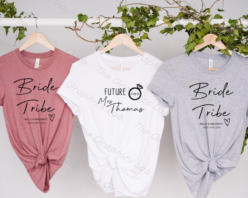 May include: Three t-shirts with text and a heart design. The pink shirt says "Bride Tribe" with the text "Kelly's Hen Party Ibiza June 2022". The white shirt says "Future Mrs Thomas" with a ring and the date "27.08.22". The grey shirt says "Bride Tribe" with the text "Kelly's Hen Party Ibiza June 2022".