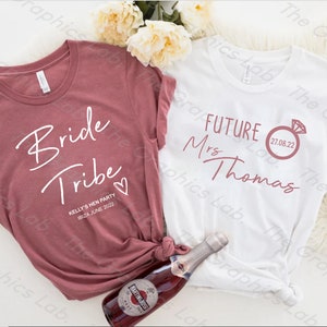 May include: Two white t-shirts with text printed on them. The shirt on the left says "Bride Tribe" with a heart and the date "08.24.JUNE 2022". The shirt on the right says "FUTURE Mrs Thomas" with a ring and the date "27.08.22".