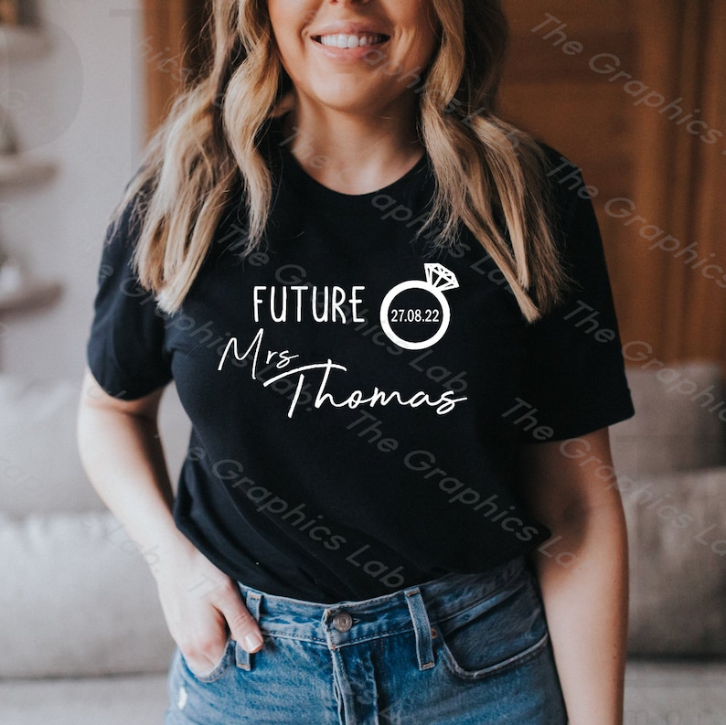 May include: Black t-shirt with white text that reads "FUTURE Mrs Thomas" and a white ring with a diamond graphic and the date "27.08.22".