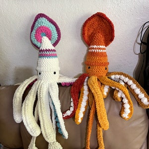 May include: Two crocheted squid plushies, one white with pink and blue accents, and one orange with white accents.