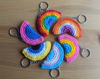 May include: A set of seven crocheted rainbow keychains, each with a different color scheme. The keychains are arranged in a circle, with the key rings facing outwards.
