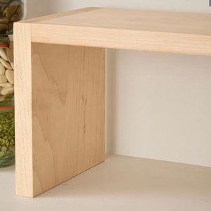 Op de afbeelding: Een lichtgekleurd houten plank met een eenvoudig, modern ontwerp. De plank is rechthoekig met een platte bovenkant en een massief zijpaneel. De houtnerf is zichtbaar en de plank lijkt onafgewerkt.
