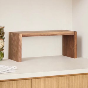 Op de afbeelding: Een houten plank met een rechthoekige bovenkant en twee verticale steunen. De plank is gemaakt van lichtbruin hout en is ontworpen om op een aanrecht te staan. De plank is ongeveer 61 cm lang en 20 cm diep.