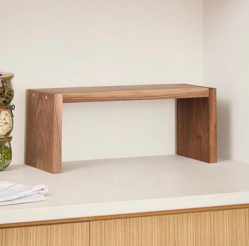 Op de afbeelding: Een houten plank met een rechthoekige bovenkant en twee verticale steunen. De plank is gemaakt van lichtbruin hout en is ontworpen om op een aanrecht te staan. De plank is ongeveer 61 cm lang en 20 cm diep.