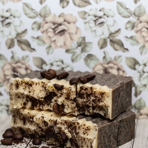 Può includere: Tre saponette fatte a mano con profumo di caffè e zucchero di canna. Il sapone è bianco con fondi di caffè marroni e chicchi di caffè in cima.