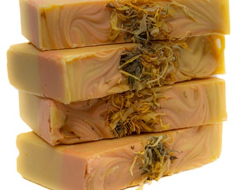 May include: Four bars of handmade soap stacked on top of each other. The soap is a light orange colour with swirls of a darker orange colour. The soap is decorated with dried herbs and flowers.