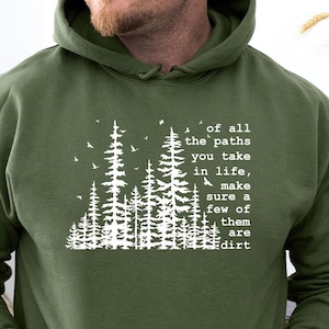 May include: An olive green hooded sweatshirt featuring a white graphic print of a forest silhouette with birds and the text: of all the paths you take in life, make sure a few of them are dirt. The hoodie includes a front kangaroo pocket.