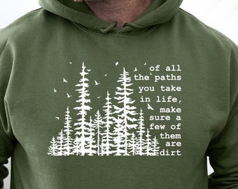 May include: An olive green hooded sweatshirt featuring a white graphic print of a forest silhouette with birds and the text: of all the paths you take in life, make sure a few of them are dirt. The hoodie includes a front kangaroo pocket.