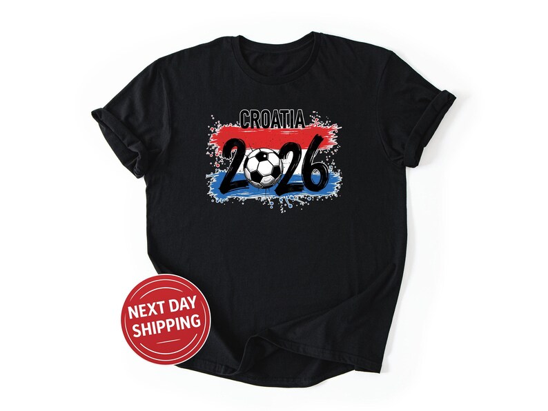 May include: Black t-shirt with a graphic featuring the word "CROATIA" above the number "2026" and a soccer ball. The design incorporates red, white, and blue colors, resembling a flag. A red and white "NEXT DAY SHIPPING" sticker is on the shirt.