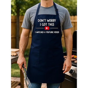 May include: Navy blue apron with the text "DON'T WORRY I GOT THIS" above a YouTube logo and the text "I WATCHED A YOUTUBE VIDEO". The apron has a front pocket and adjustable neck strap.