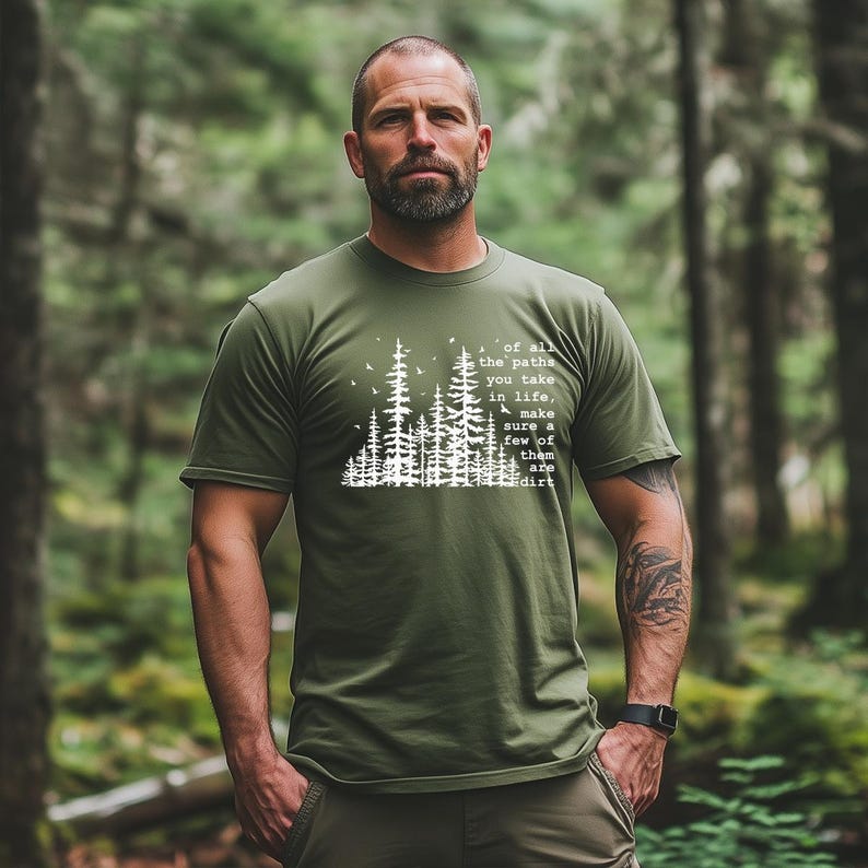 May include: An olive green short-sleeved t-shirt featuring a white graphic of a forest silhouette with birds and the text: of all the paths you take in life, make sure a few of them are dirt. The shirt has a crew neckline and a standard fit.