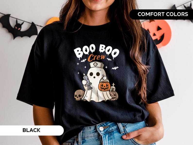 May include: Black t-shirt with a Halloween-themed graphic. The design features a ghost wearing a nurse's cap and holding a syringe and a jack-o'-lantern. The text "BOO CREW" is above the ghost. Two skulls and pumpkins are also in the design.