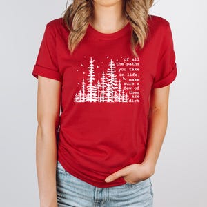 May include: A red short-sleeved t-shirt featuring a white graphic of pine trees and birds. The text reads: Of all the paths you take in life, make sure a few of them are dirt. The shirt has a crew neckline and rolled sleeves.