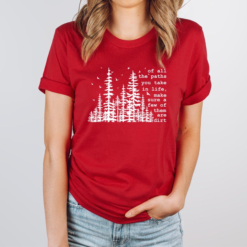 May include: A red short-sleeved t-shirt featuring a white graphic of pine trees and birds. The text reads: Of all the paths you take in life, make sure a few of them are dirt. The shirt has a crew neckline and rolled sleeves.