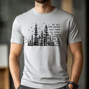 May include: A light gray short-sleeved t-shirt featuring a black graphic of a pine forest with birds and the text: of all the paths you take in life, make sure a few of them are dirt. The shirt has a crew neckline and a standard fit.