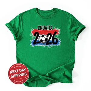 May include: Green t-shirt with the word "CROATIA" above the numbers "2026" and a soccer ball graphic. The design incorporates red, white, and blue colors, and the shirt has short sleeves.